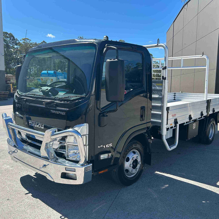 Black truck with a flatbed on a concrete surface under a blue sky.